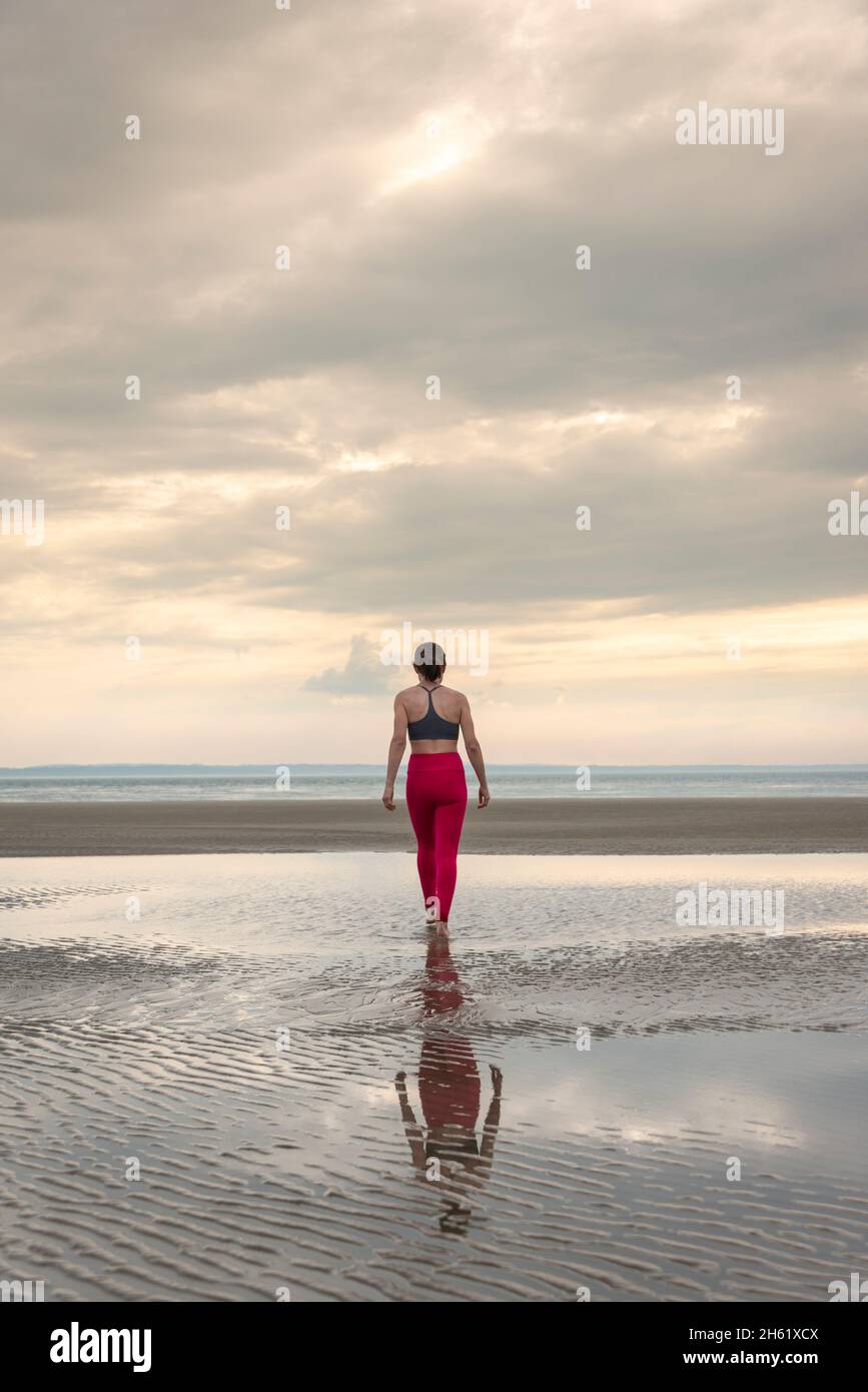 Donna che cammina su una spiaggia in abiti da ginnastica, vista posteriore. Foto Stock