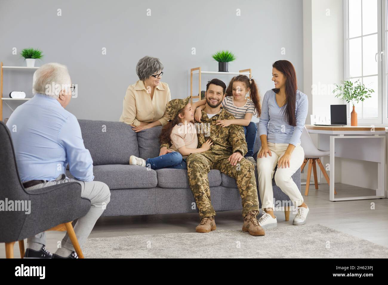 Felice soldato che è tornato a casa dal servizio militare seduto sul divano con la sua famiglia Foto Stock