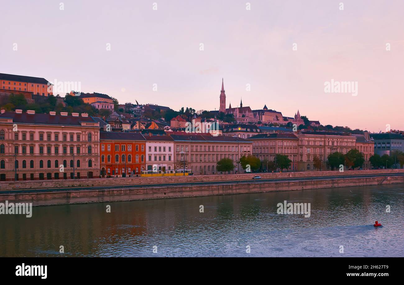 Goditi la vista dell'ora d'oro del quartiere di Buda dal Danubio con l'alta guglia della Chiesa di Mattia, che domina la collina del Castello, gli edifici storici A. Foto Stock