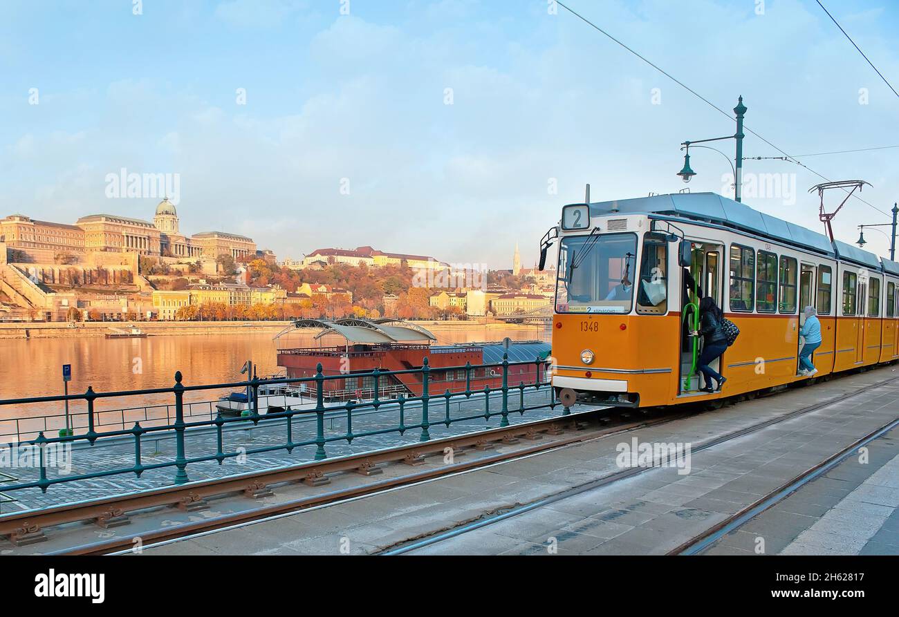 Il tram giallo d'epoca si è fermato sulla stazione di Belgrado Quay con una via vinta Danubio e il Castello di Buda sulla riva opposta, Budapest, Hungar Foto Stock