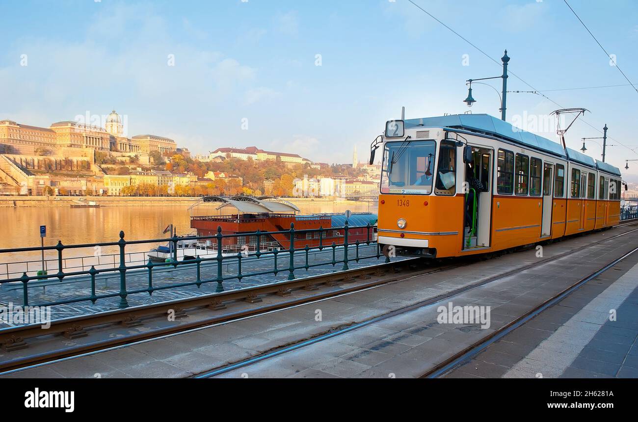 Il tram giallo retrò sul Quay di Belgrado contro il Danubio e il Castello di Buda, visto sullo sfondo in luce solare, Budapest, Ungheria Foto Stock