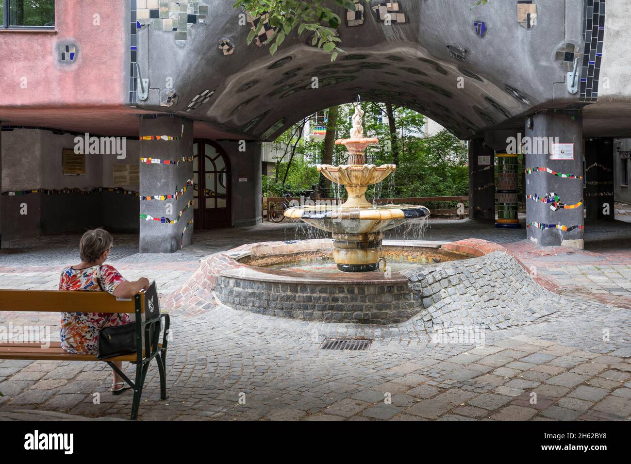 una donna si siede su una panchina presso la hundertwasserhaus presso la fontana, löwengasse angolo kegelgasse, 3 ° distretto, landstrasse, vienna, austria Foto Stock