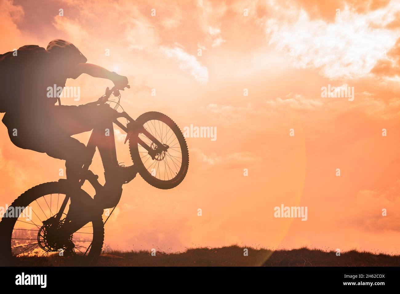 wheelie con e-bike con cielo al fuoco al tramonto,un uomo di 37 anni,dolomiti,belluno,italia Foto Stock