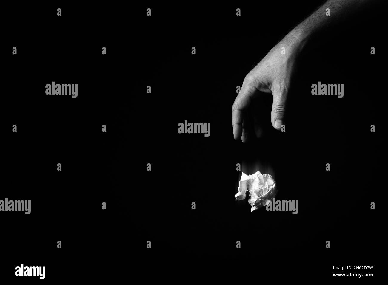 Immagine B+W della mano maschile che cade la palla di carta sbriciolita su sfondo nero con un'illuminazione spettacolare. Foto Stock