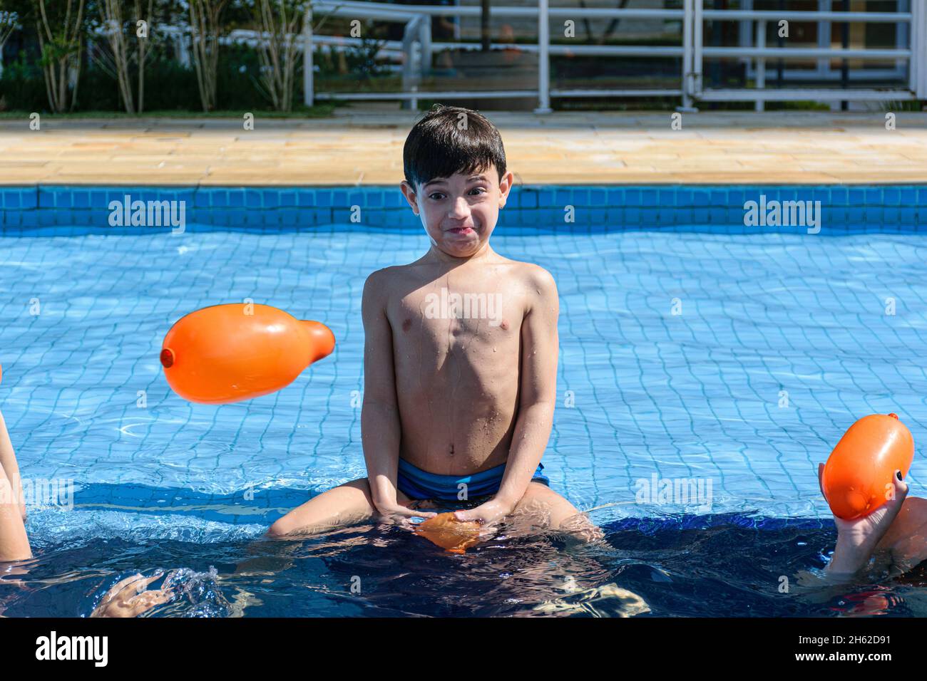 bambino di 8 anni seduto sul bordo della piscina e fare una faccia divertente. Foto Stock