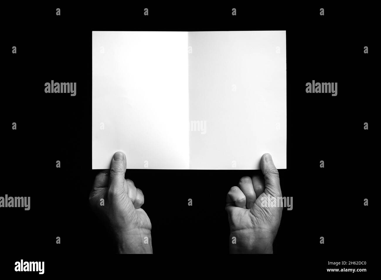 Immagine B+W delle mani maschili che tengono un foglio di carta o un cartoncino  piegato su sfondo nero con spazio per la copia Foto stock - Alamy