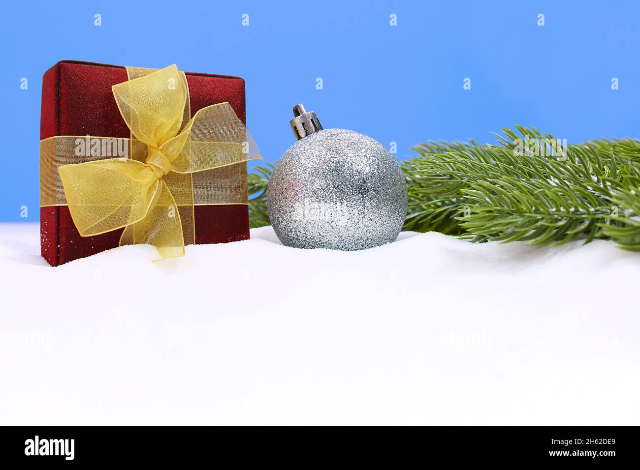 Sfera scintillante in argento con scatola presente in rami di neve e abete verde su sfondo blu con posto per il testo. Natale, Capodanno. Spazio di copia Foto Stock