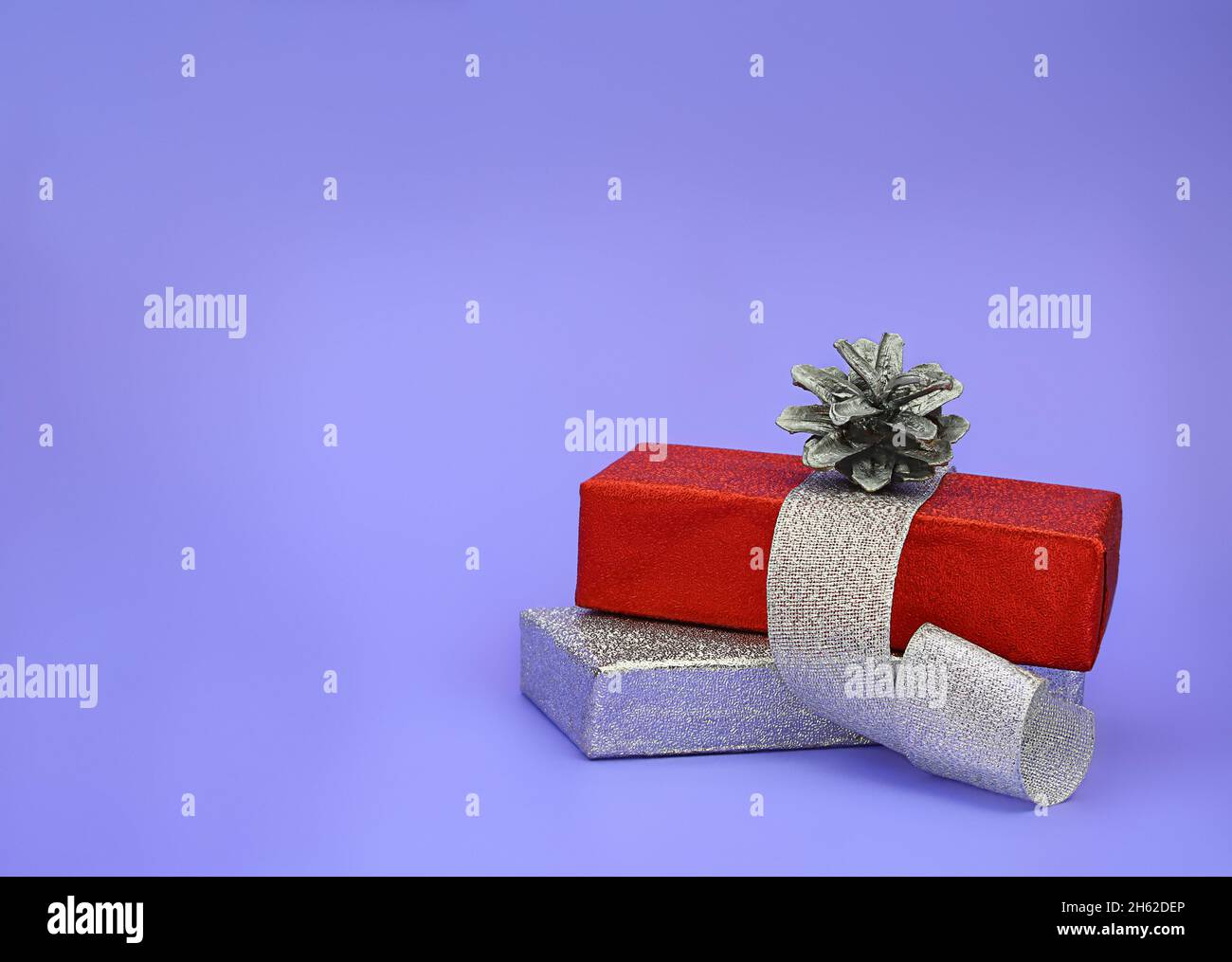 Confezione regalo in argento lucido e rosso con nastro e cono di pino. Natale, Capodanno. Spazio di copia Foto Stock