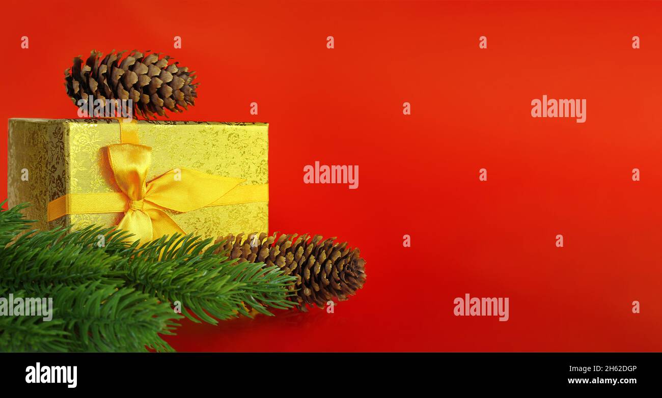 Grande scatola dorata con coni di pino e rami di abete su sfondo rosso con posto per il testo. Natale, Capodanno. Spazio di copia Foto Stock