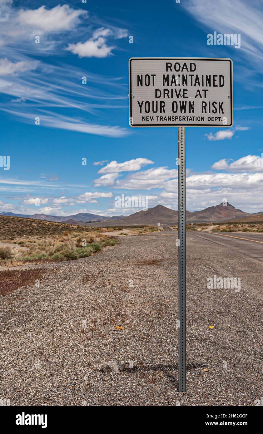 Tonopah, Nevada, Stati Uniti - 16 maggio 2011: Primo piano del cartello stradale avvertimento strada non è mantenuto, guidare a proprio rischio contro il paesaggio blu. Montagna grigia Foto Stock