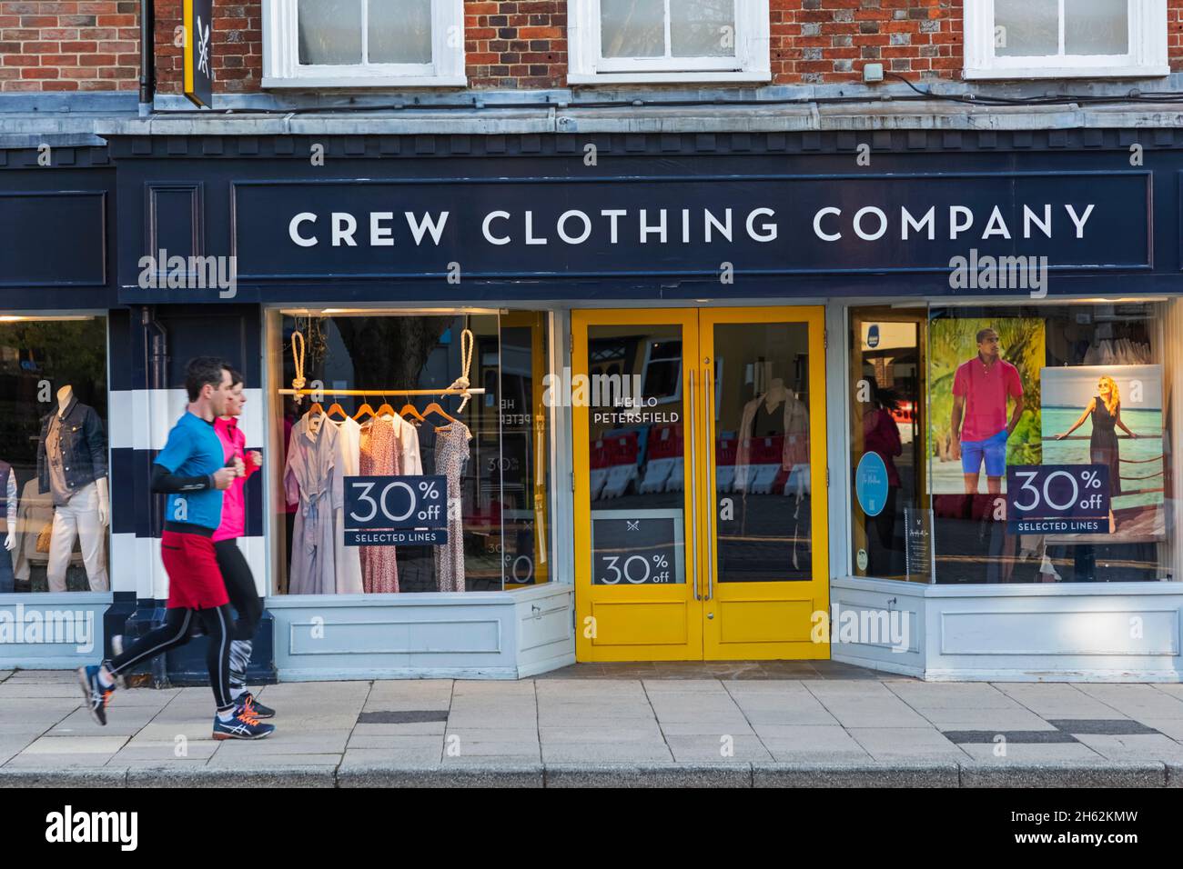 inghilterra, hampshire, petersfield, coppia jogging oltre equipaggio negozio di abbigliamento aziendale fronte Foto Stock