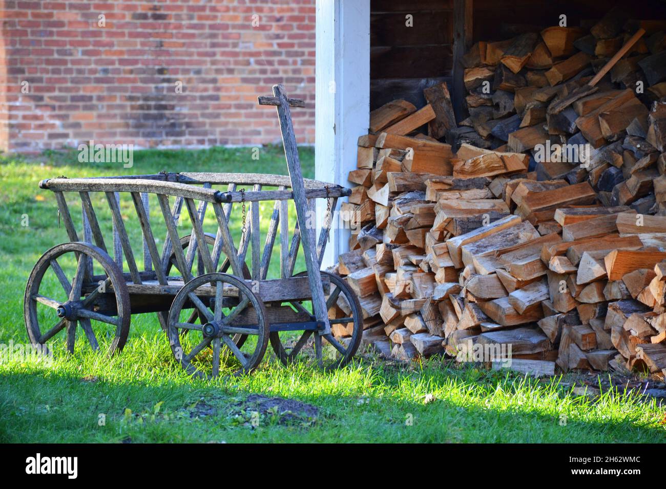 Un vecchio carro di legno accanto a una pila di legna da ardere ben impilata in una giornata di sole Foto Stock