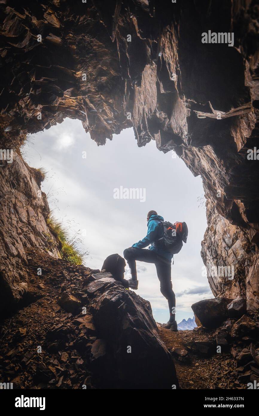 uomo solitario,30-35 anni,escursionista in controluce all'ingresso di una grotta in montagna,col di lana,dolomiti,livinallongo del col di lana,belluno,veneto,italia Foto Stock