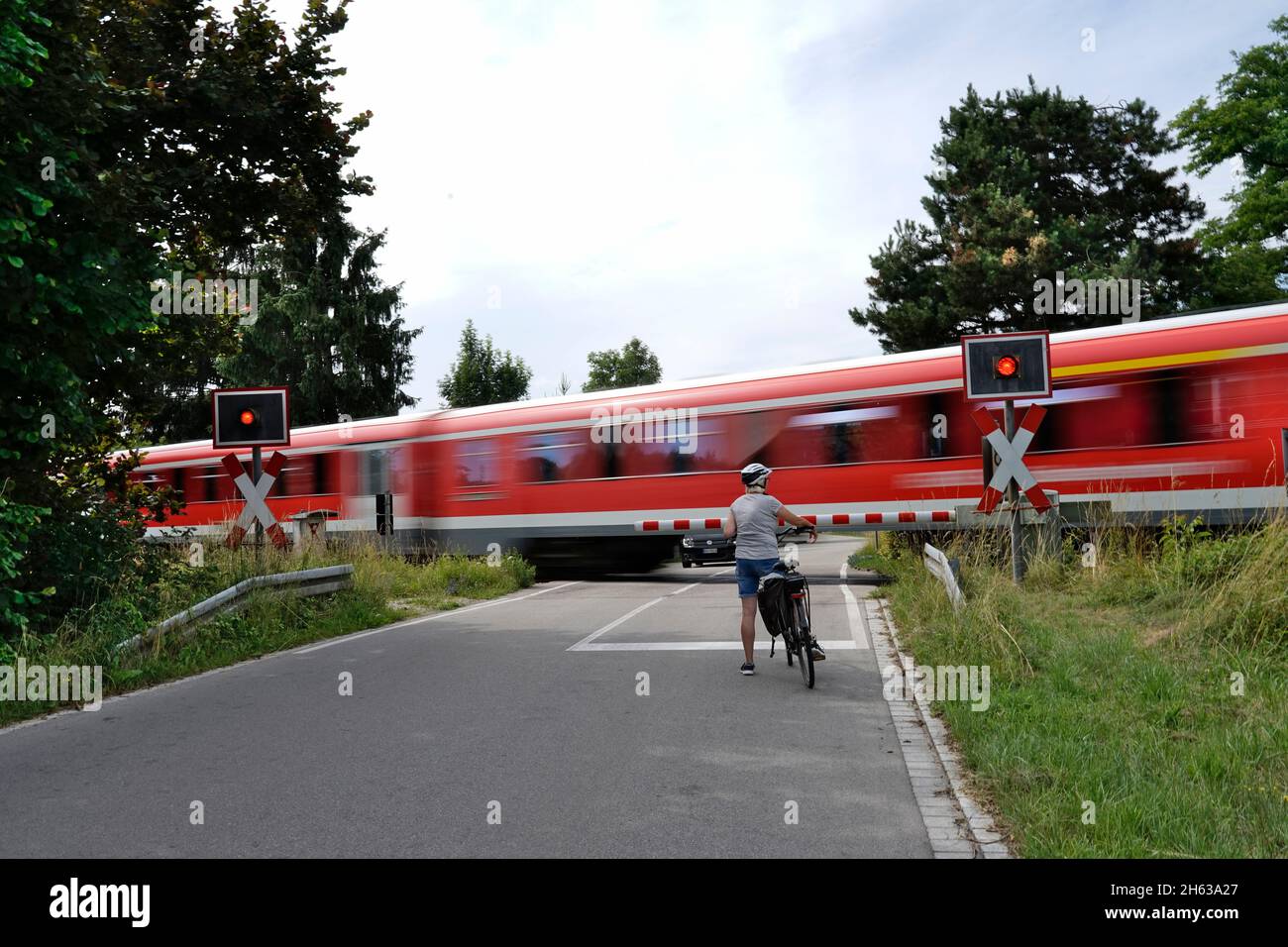 germania,baviera,alta baviera,neuötting,strada di campagna,attraversamento a livello limitato,ciclisti in attesa,treno locale che passa attraverso Foto Stock