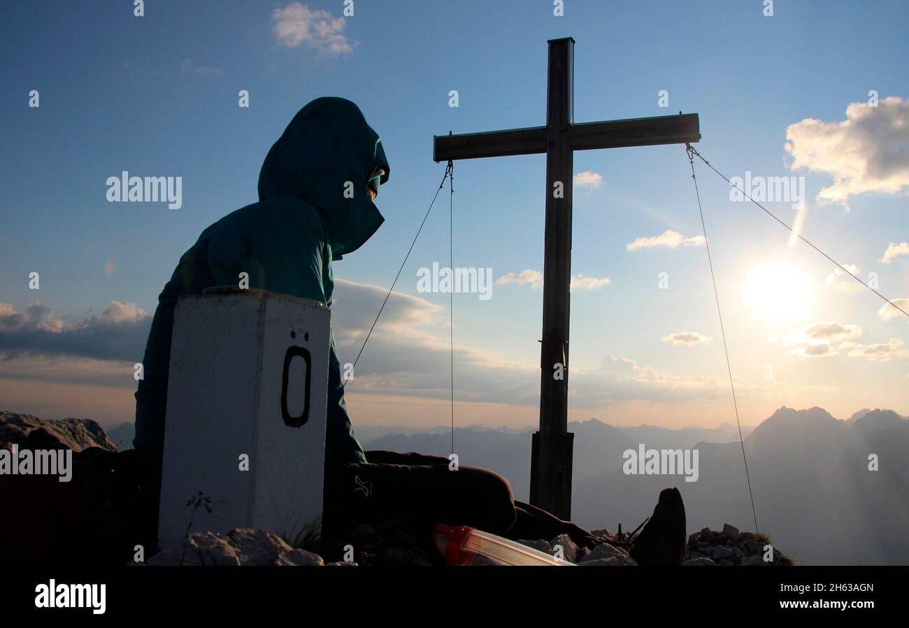 giovane donna a riposo, croce di montagna all'alba, pietra di confine germania, austria, escursione, obere wettersteinspitze, 2.297 m germania, baviera, alta baviera, werdenfelser terra, mittenwald, valle isar Foto Stock