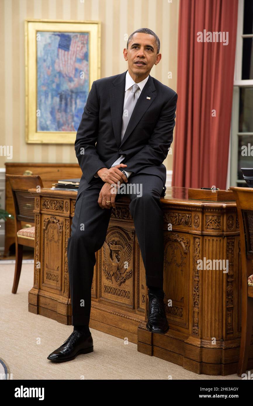 Il presidente Barack Obama siede sul bordo del Resolute Desk durante una riunione presso l'Oval Office, il 19 dicembre 2012. Foto Stock