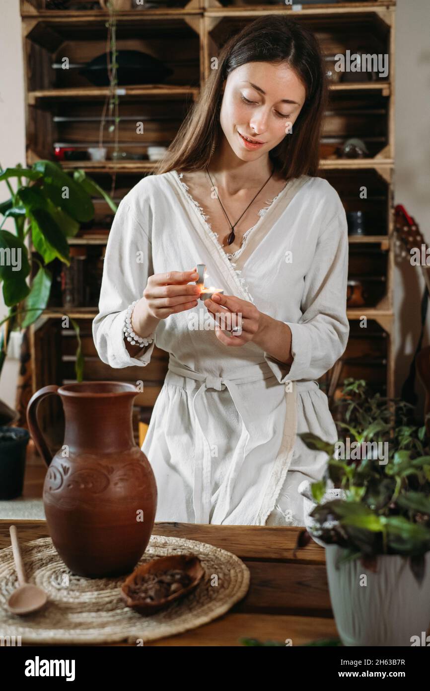Cerimonia del cacao in uno spazio atmosferico con piante verdi e candele. Donna che fa la bevanda rituale sana dai fagioli di cacao Foto Stock