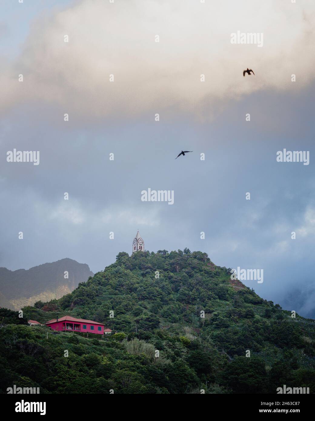 cielo serale a madeira. cappella su una collina boscosa e 2 uccelli nel cielo. Foto Stock