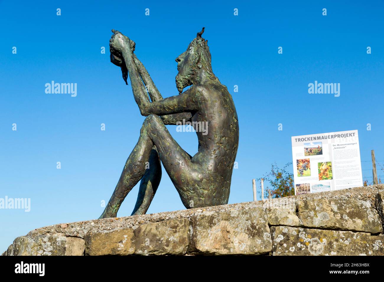 germania,baden-wuerttemberg,kernen im remstal,lo spirito del vino si trova sulla parete di pietra asciutta sul burgsteige a yburg con vista sul villaggio del vino di stetten, la "porta di accesso al remstal". l'artista dello spirito metallo-plastica, chiamato anche deifele o teufelchen, è karl ulrich nuss. Foto Stock