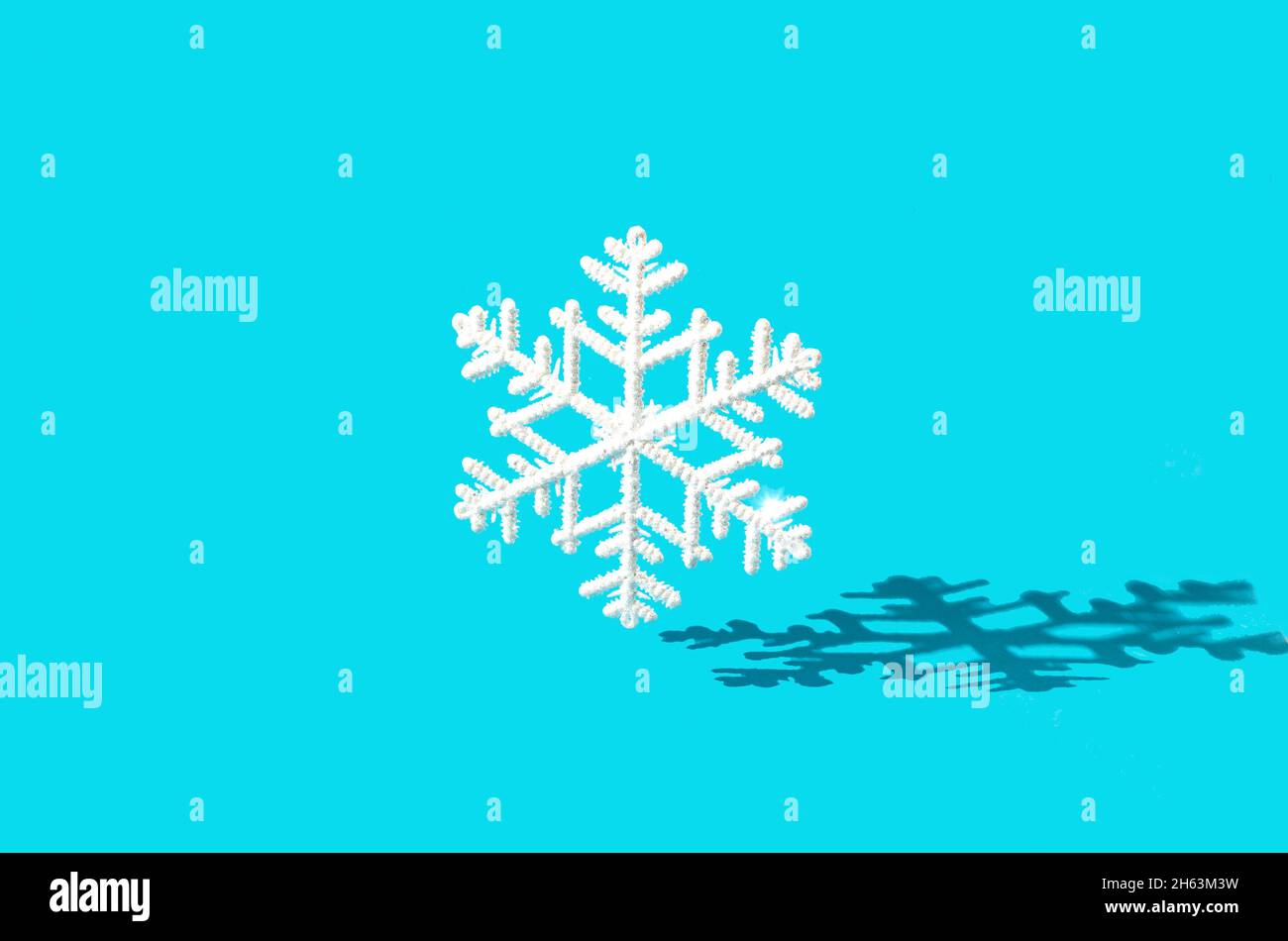 Un grande fiocco di neve bianco che cade su uno sfondo blu pastello con una forte ombra. Design creativo minimo per la stagione invernale. Banner o pubblicità per Chris Foto Stock