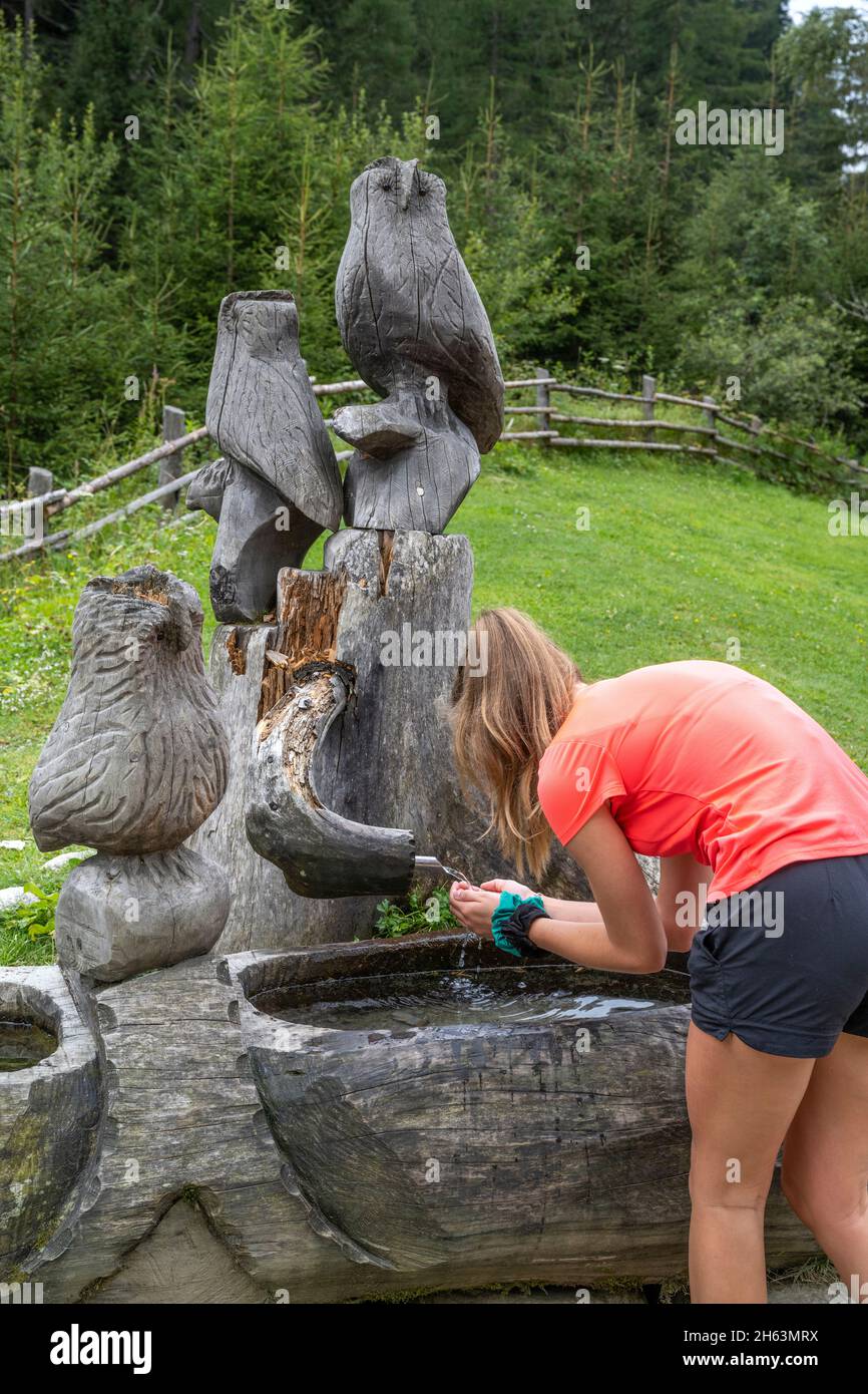anterselva, provincia di bolzano, alto adige, italia. una ragazza beve acqua da un pozzo sul lago di anterselva Foto Stock