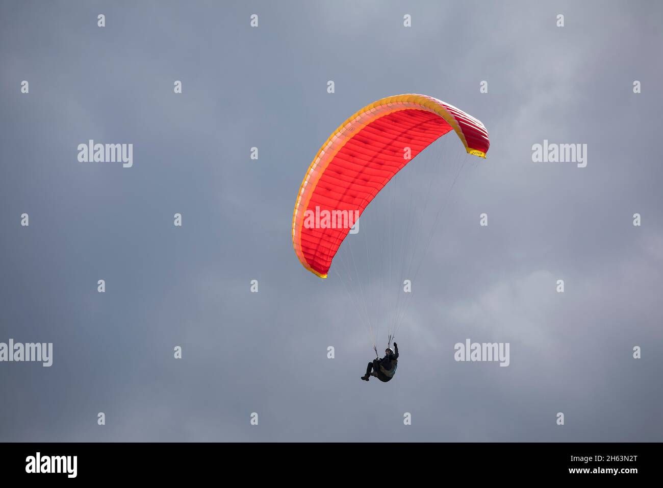 parapendio con ombrello rosso di fronte a un cielo coperto, sopra sillian in hochpustertal, tirolo orientale, distretto di lienz, tirolo, austria Foto Stock