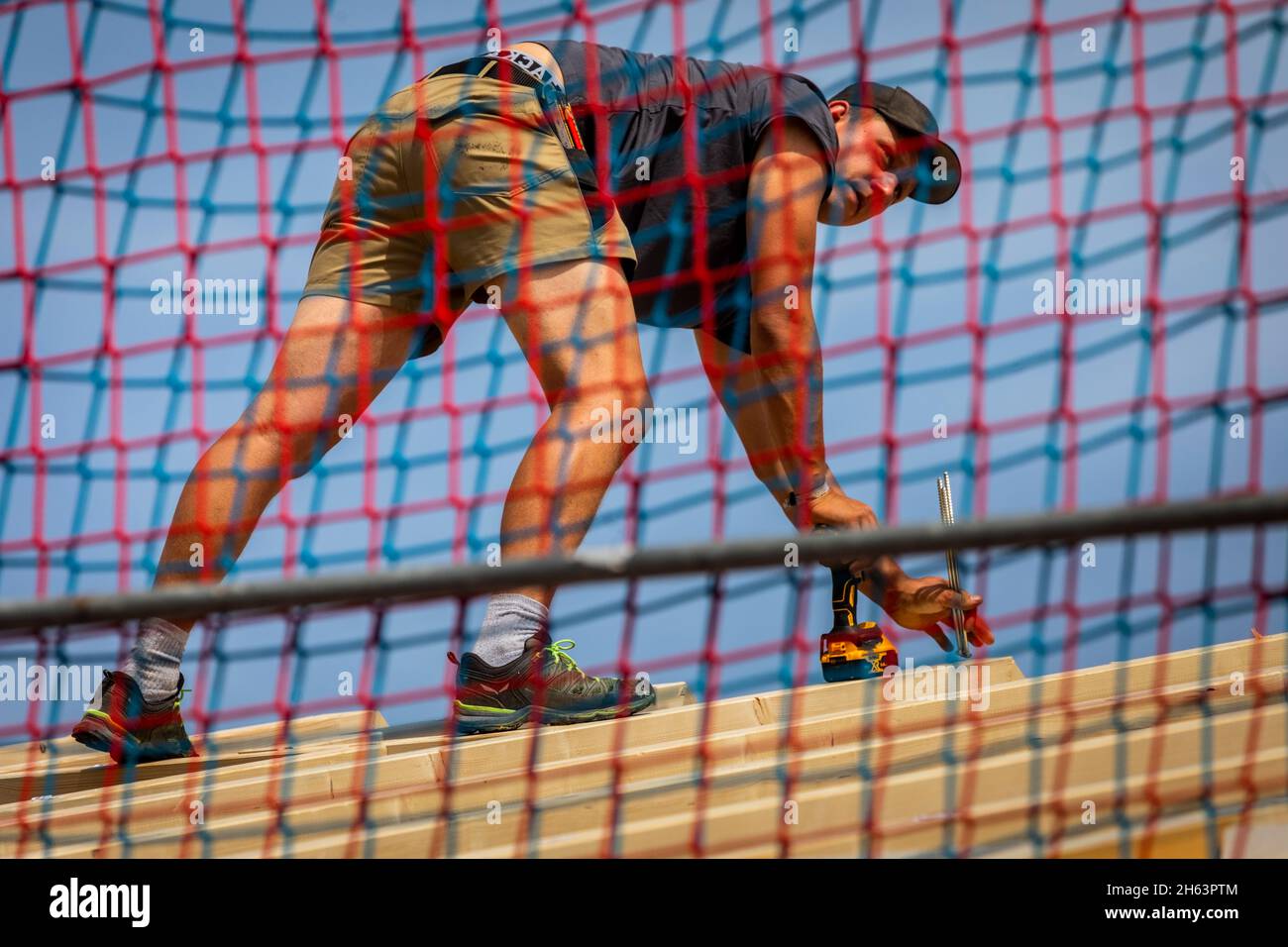 germania,baviera,costruzione di una casa prefabbricata in legno,carpentiere con avvitatore a batteria dietro la rete di sicurezza, Foto Stock