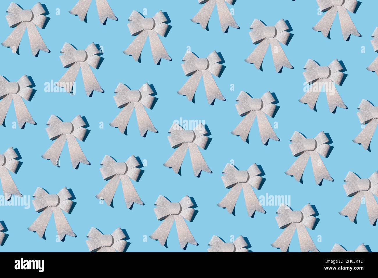 Motivo a nastro ad arco in argento brillante su sfondo blu pastello. Natale e Capodanno decorazione idea. Minimo concetto di vacanze invernali. Disposizione piatta Foto Stock