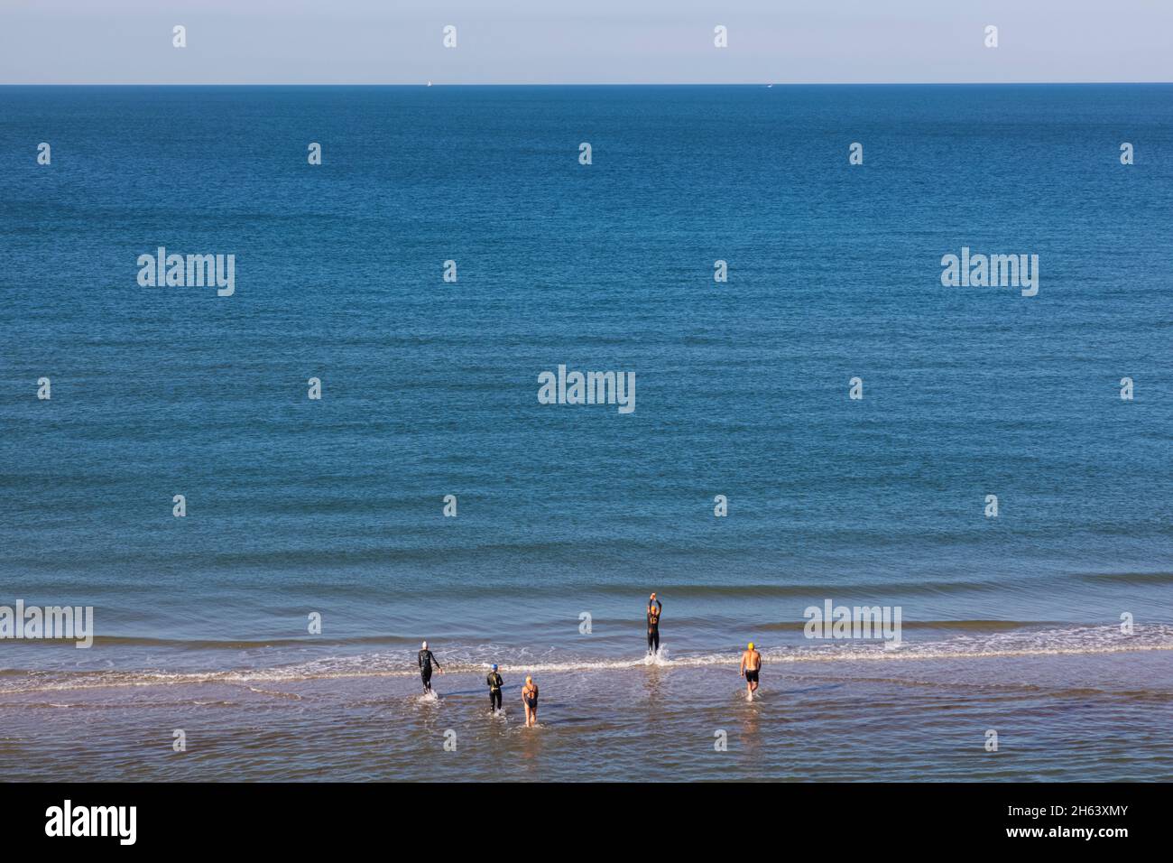 inghilterra,hampshire,la nuova foresta,milford-on-sea beach,gruppo di nuotatori che entrano in mare calmo con orizzonte vuoto Foto Stock