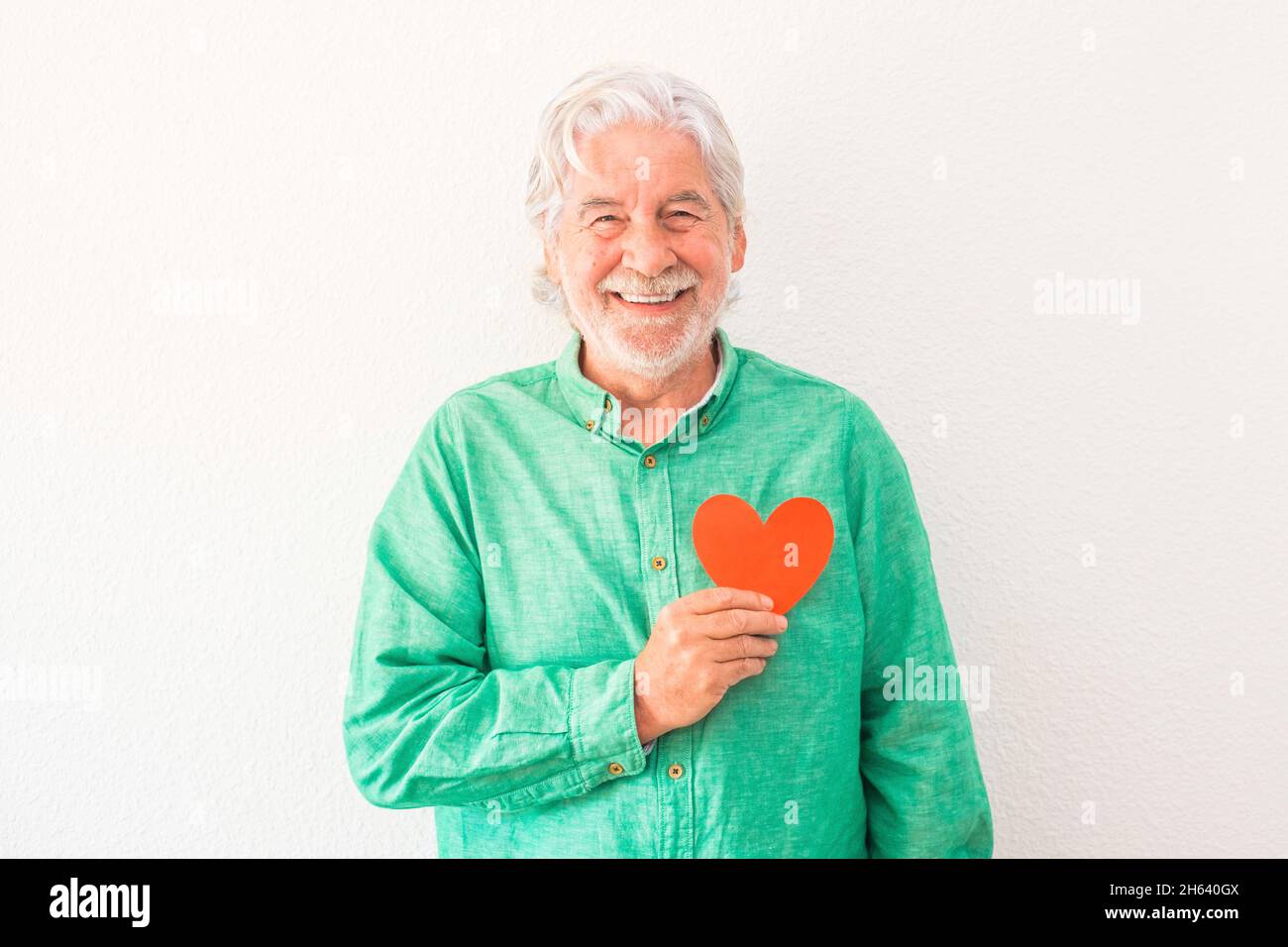 ritratto di un uomo maturo sorridente e guardando la macchina fotografica con un cuore rosso sul petto - uomo con problemi cardiaci e concetto di malattia Foto Stock ritratto di un uomo maturo sorridente e guardando la macchina fotografica con un cuore rosso sul petto - uomo con problemi cardiaci e concetto di malattia Foto Stock
