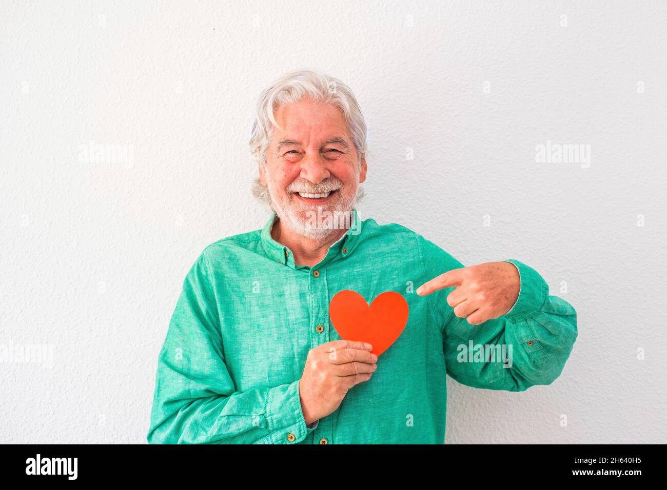 ritratto di un uomo maturo sorridente e guardando la macchina fotografica con un cuore rosso sul petto - uomo con problemi cardiaci e concetto di malattia Foto Stock