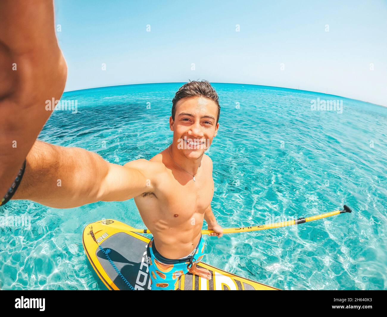 un felice uomo caucasico godendo e divertirsi in vacanza all'aperto in spiaggia a cavallo di una paddle surf in acqua. ragazzo attraente sensazione di viaggiare libero. Foto Stock