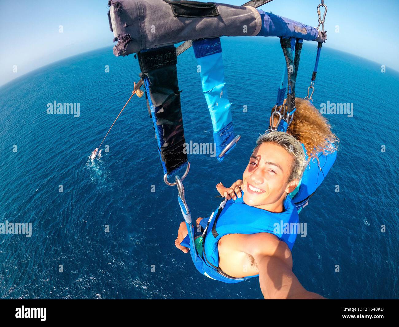 coppia di due persone felici godendo l'estate e le vacanze facendo attività estreme sul mare con una barca - persone belle prendendo un selfie mentre facendo paracadutismo insieme Foto Stock