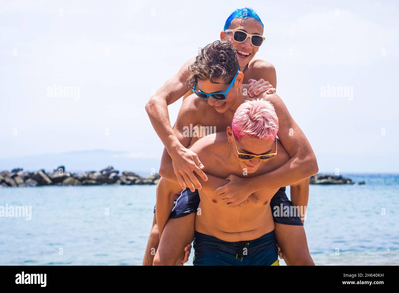 gruppo di ragazzi allegri e colorati che si divertono e si divertono in spiaggia durante l'estate giocando sulla sabbia. tre giovani caucasici sorridenti Foto Stock