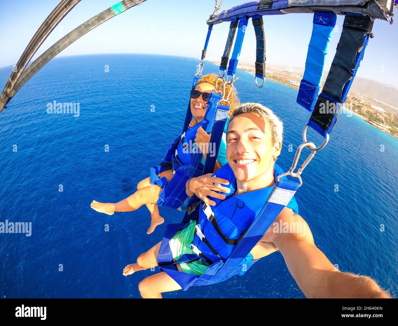 coppia di due persone felici godendo l'estate e le vacanze facendo attività estreme sul mare con una barca - persone belle prendendo un selfie mentre facendo paracadutismo insieme Foto Stock