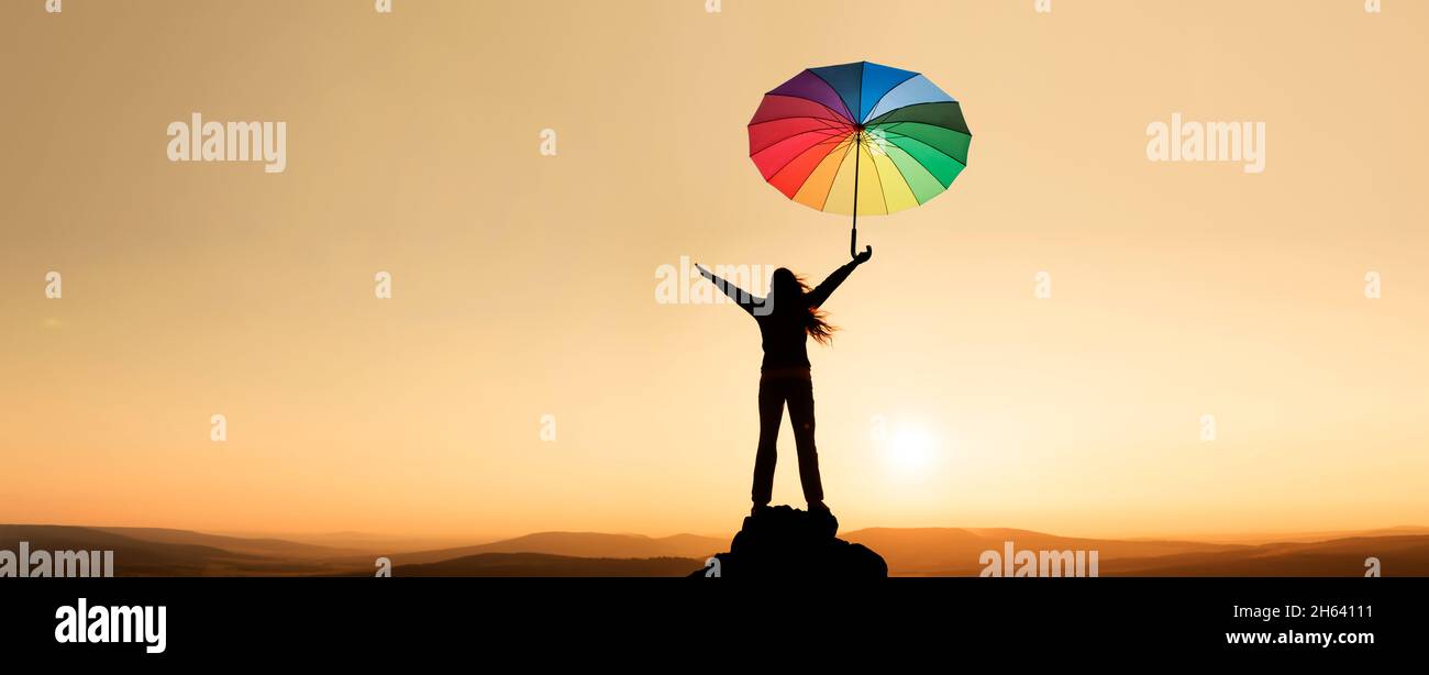 donna in un paesaggio con braccia sparse e un ombrello colorato Foto Stock