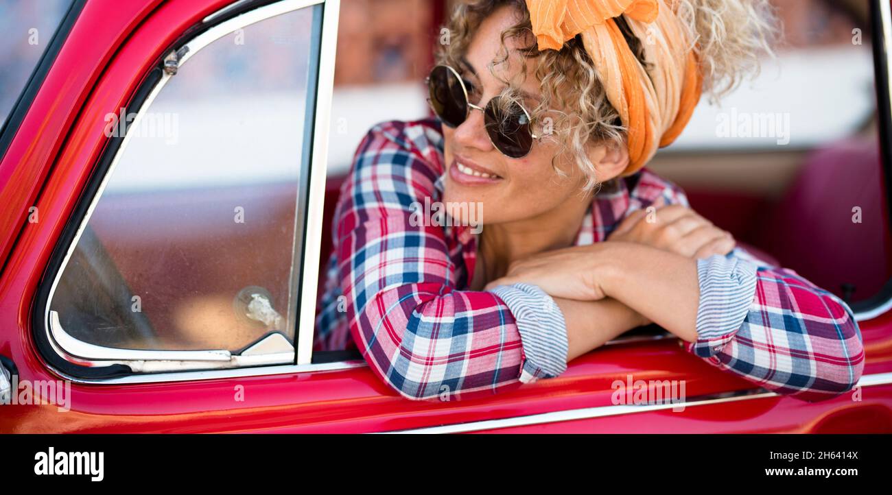 felice allegro giovane donna adulta sorriso e godere seduto all'interno della sua auto rossa alla moda pronto per iniziare e guidare via per un viaggio o una vacanza - gioioso stile di vita femminile persone indipendenti Foto Stock