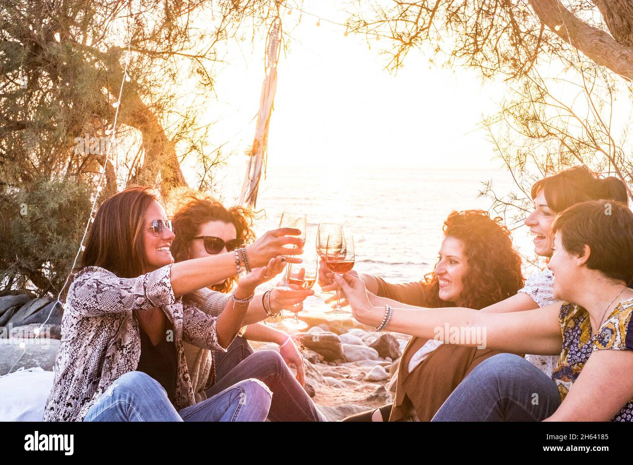 amici femmina gente giovane adulto divertirsi e godere insieme clinking con vino rosso all'aperto - spiaggia e sfondo tramonto con le donne sorridenti e bere insieme Foto Stock