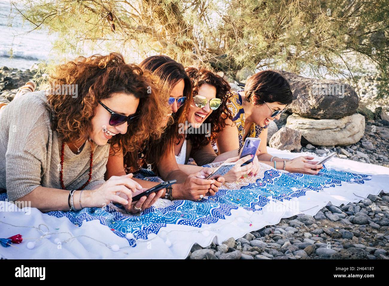 gruppo di giovani donne adulte usano i telefoni moderni insieme avendo divertimento e ridendo mólto - gente felice delle femmine che gode della tecnologia e della connessione del internet laydown esterno Foto Stock