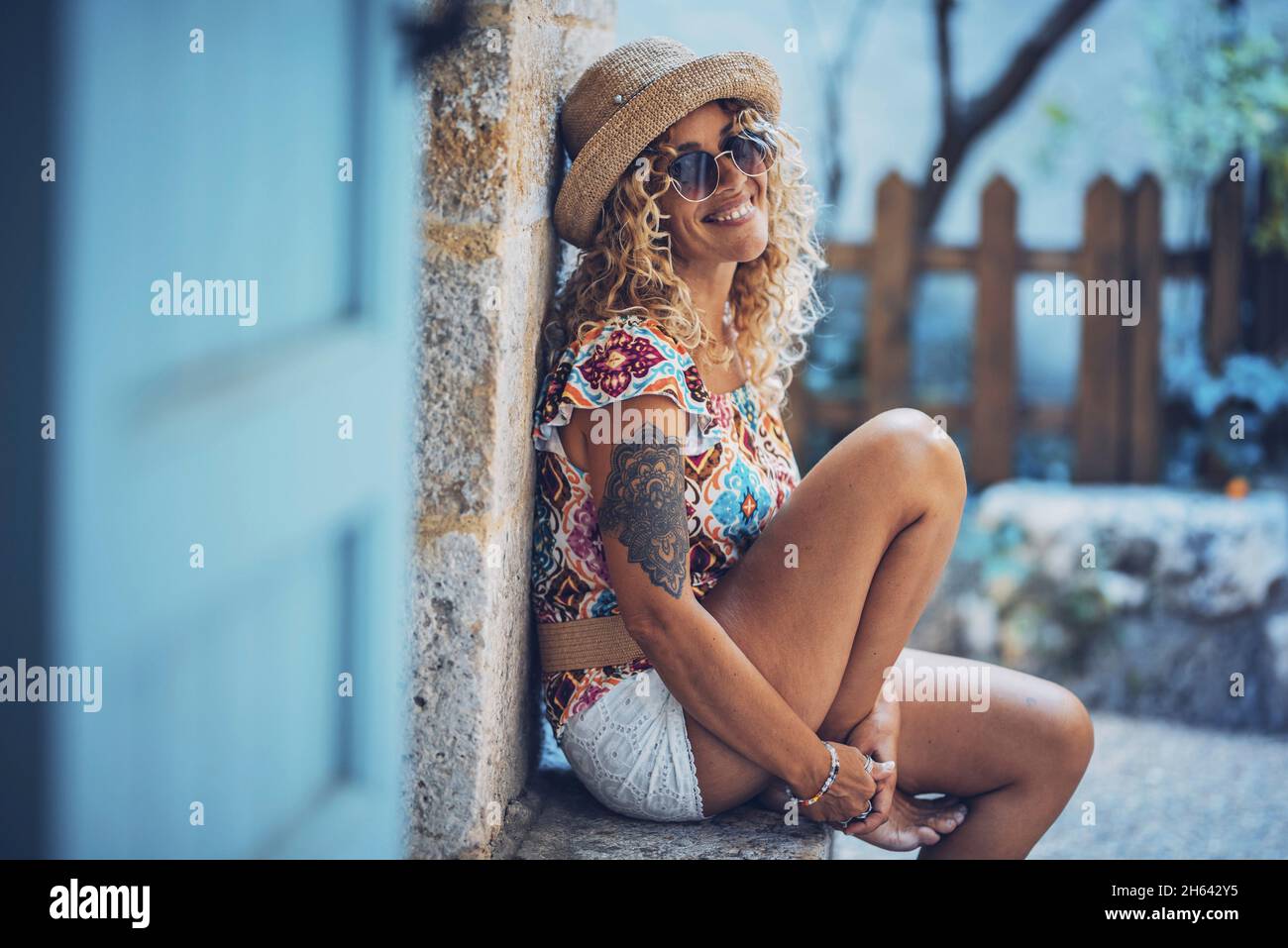 ritratto di bella sorridente ippica giovane donna in occhiali da sole e cappello di paglia seduta all'aperto. elegante donna tatuata di buon umore trascorrere il tempo libero rilassarsi all'aperto Foto Stock