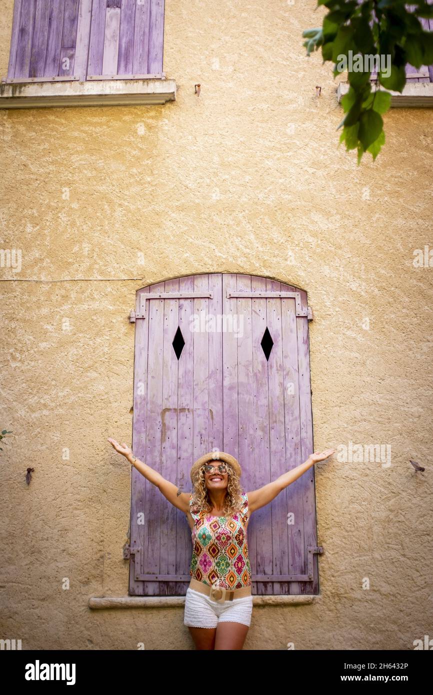 spensierate bella donna in paglia cappello in piedi con le sue braccia larghe distese di fronte a vecchio legno porta chiusa di muro di costruzione testurizzata. donna hipster godere di libertà all'aperto in vacanza. Foto Stock