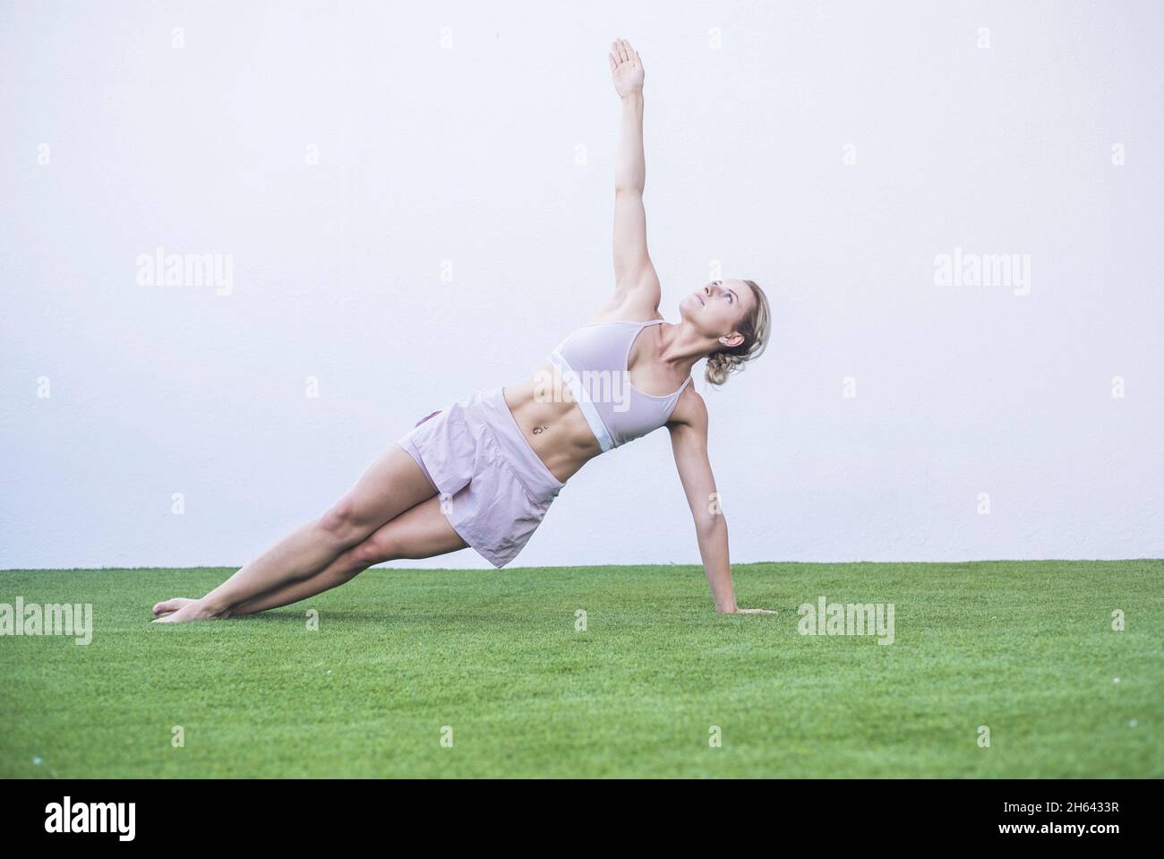 bella giovane donna che fa esercizio stretching su erba in giardino. donna in equilibrio sportivo mentre fa esercizio. sportiva giovane donna che pratica yoga all'aperto su erba verde Foto Stock