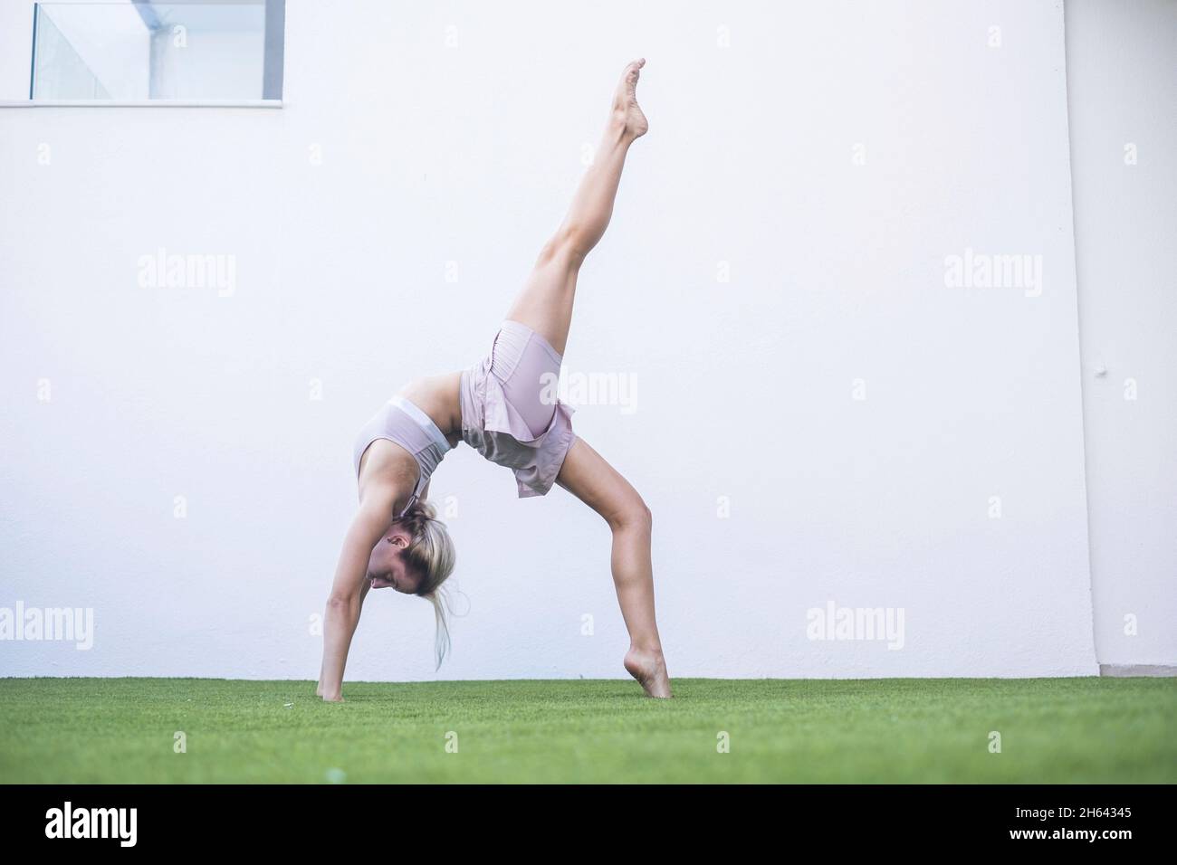 bella giovane donna che fa esercizio stretching su erba in giardino. donna in equilibrio sportivo mentre fa yoga. adatta giovane donna che pratica yoga posa su erba verde Foto Stock