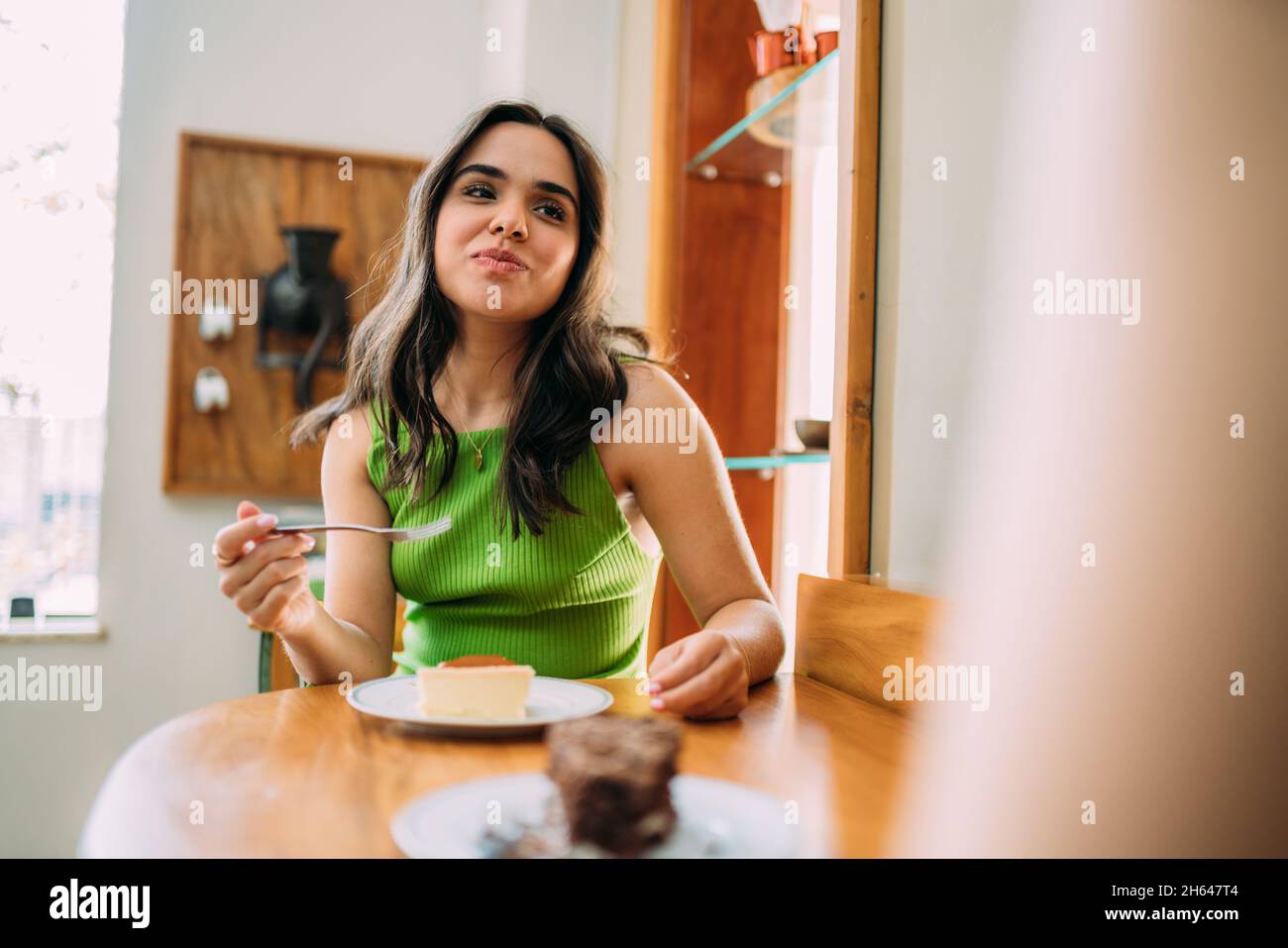 Giovane ragazza latina seduta in caffè mangiare torta Foto Stock