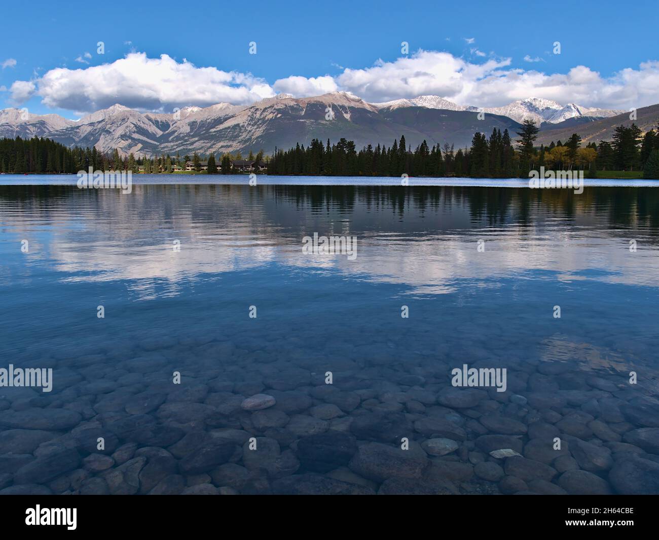 Splendida vista sul lago Beauvert a Jasper, Alberta, Canada, con riflessi nelle acque pianeggianti e pietre rotonde sulla riva in giornata di sole in autunno. Foto Stock