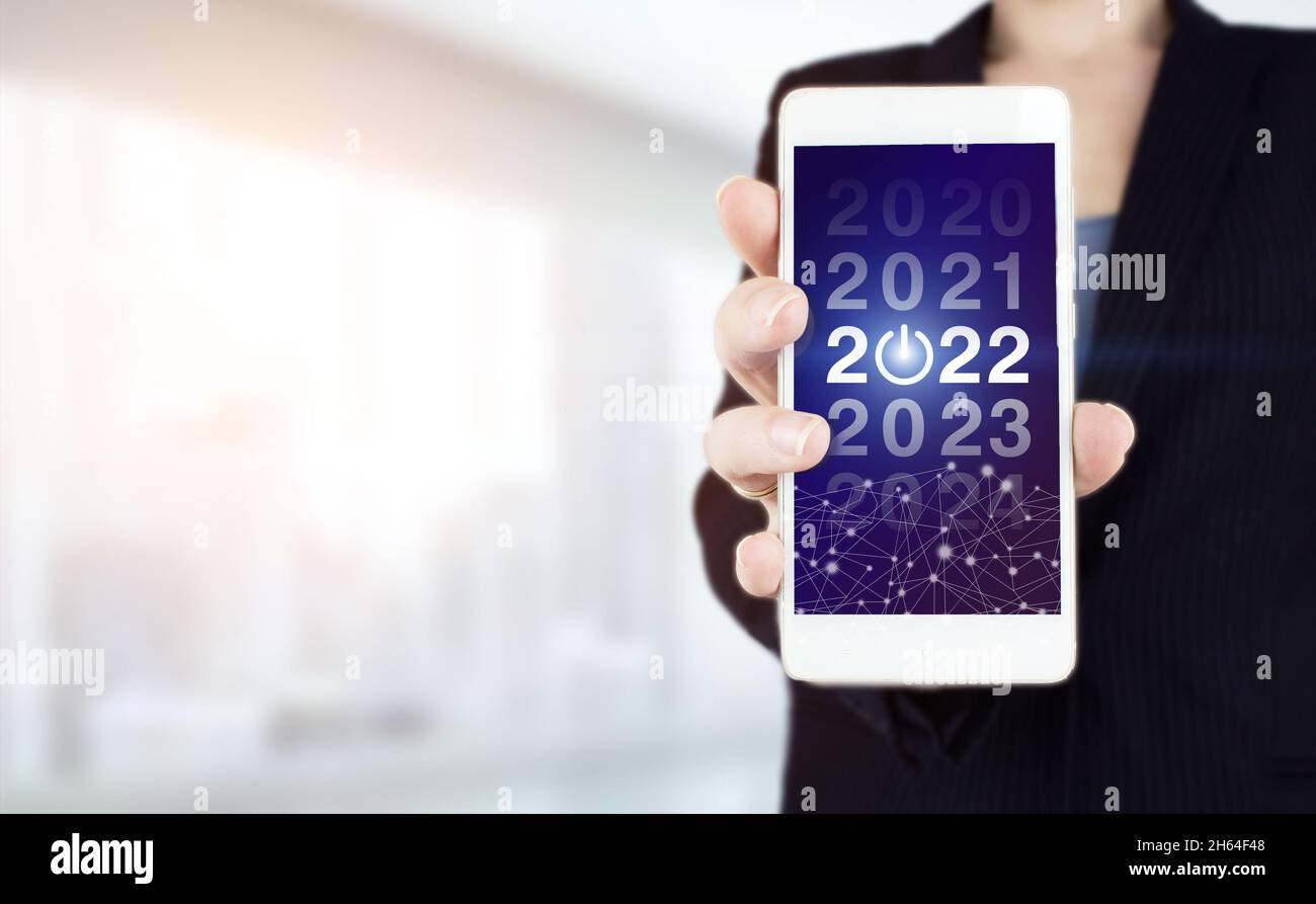 Concetto di successo per il nuovo anno. Gestione aziendale, idee sui concetti di ispirazione. Smartphone bianco portatile con ologramma digitale 2022 segno su chiaro sfocato Foto Stock