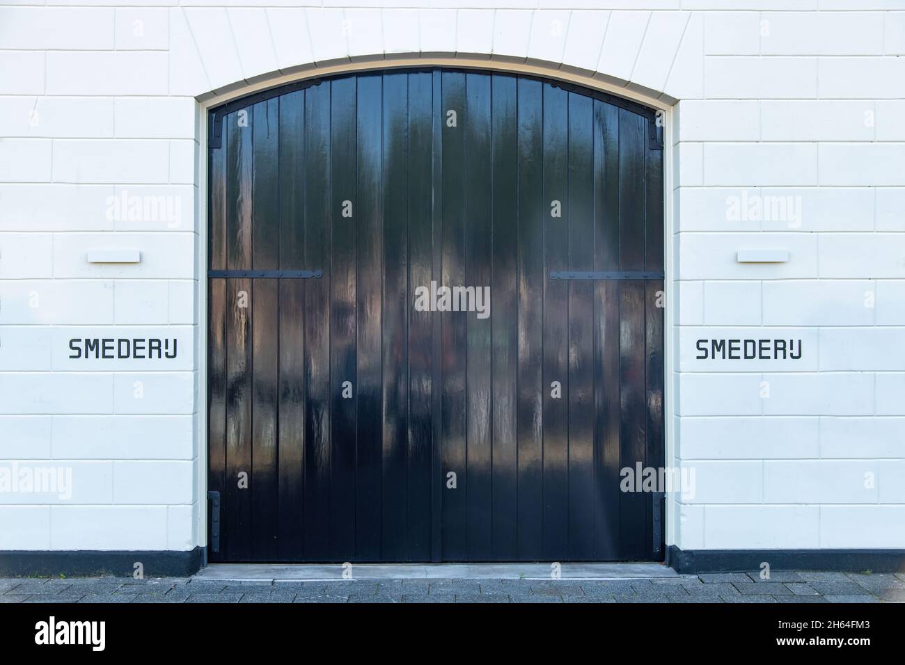 Primo piano della facciata splendidamente rinnovata di un ex smithy (Smederij traduce da olandese) con grandi pareti di pietra bianca e grandi porte e parole Foto Stock