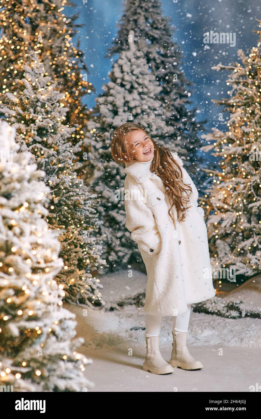 carina ragazza bionda caucasica in cappotto bianco eco pelliccia camminare nella foresta di natale inverno con le luci. Anno nuovo, concetto di fiaba Foto Stock