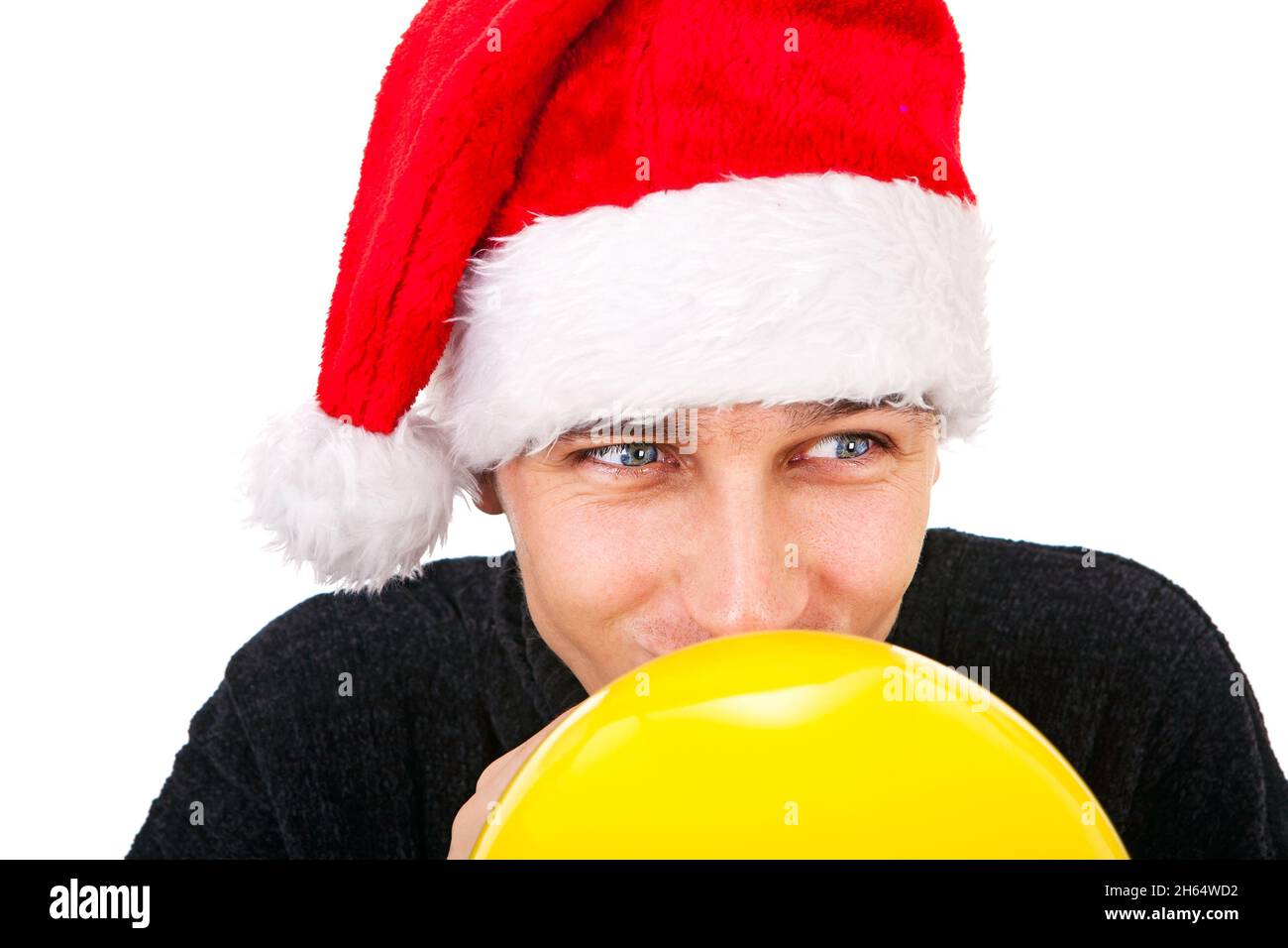Giovane uomo a Santa Hat gonfiare un pallone giallo isolato sullo sfondo bianco Foto Stock