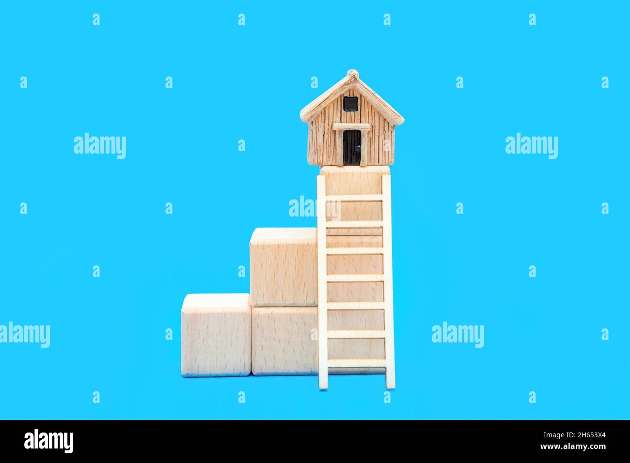 Scala giocattolo che conduce ad una piccola casa sulla parte superiore di blocchi di legno impilati isolati su uno sfondo blu. Il concetto di salire su una scala di proprietà. Foto Stock